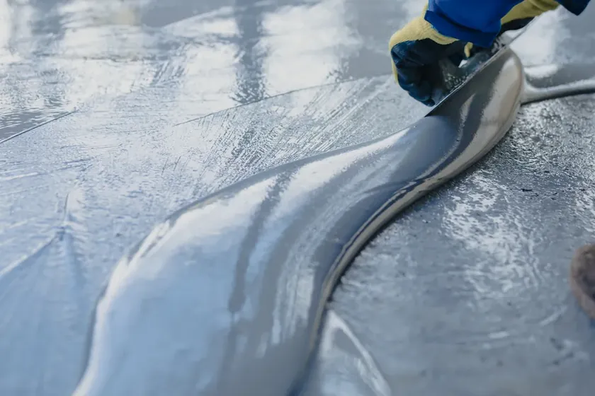 A floor coating being spread across prepared concrete with a trowel.